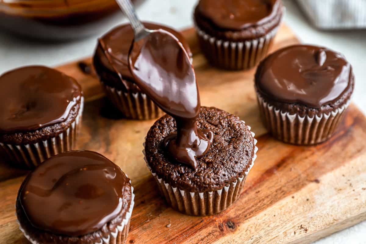 Ganache poured over chocolate cupcakes.