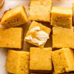 Cornbread squares with butter and honey on a baking sheet.