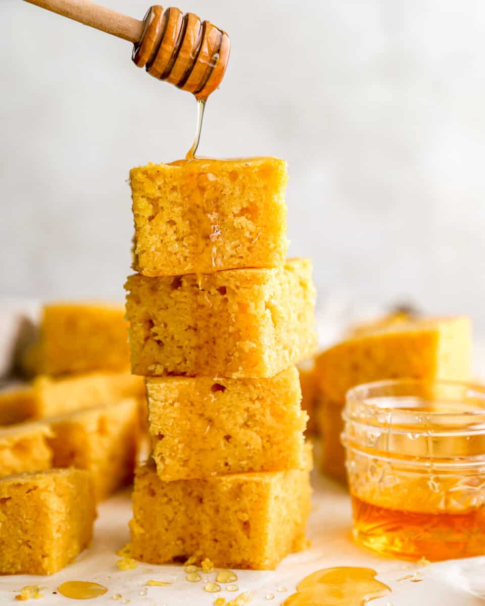 Drizzling honey over a stack of cornbread squares.