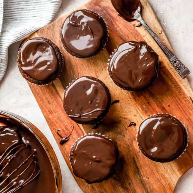 Chocolate cupcakes with chocolate ganache on a wooden cutting board.
