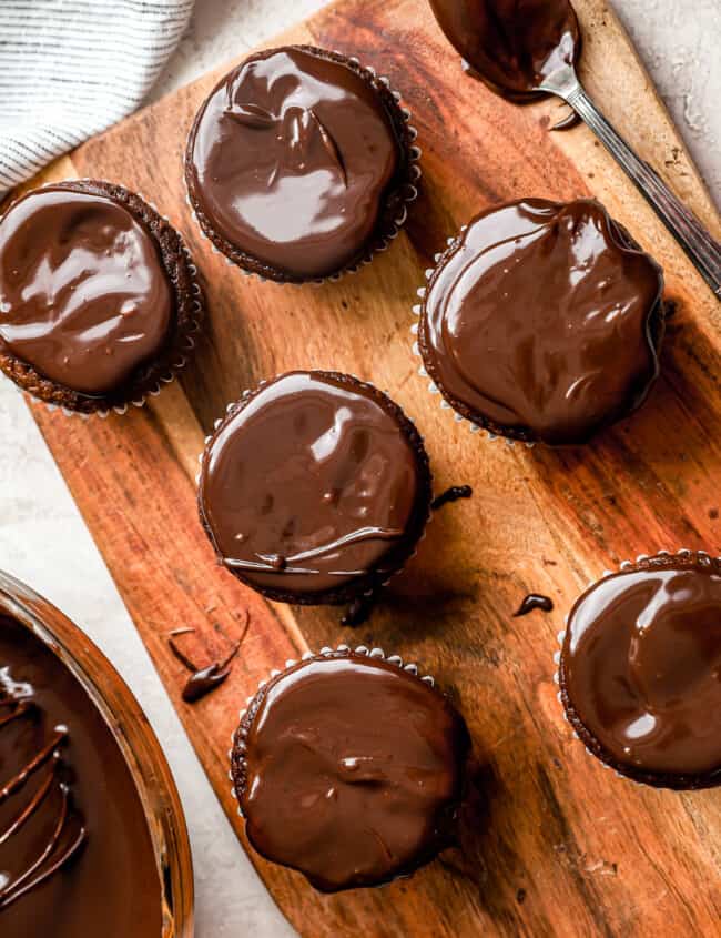 Chocolate cupcakes with chocolate ganache on a wooden cutting board.