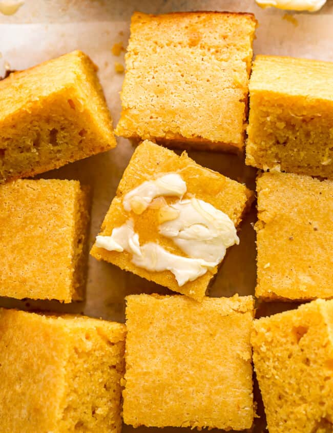 Cornbread squares with butter and honey on a baking sheet.