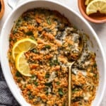 A dish of spinach and artichoke casserole with lemon wedges.