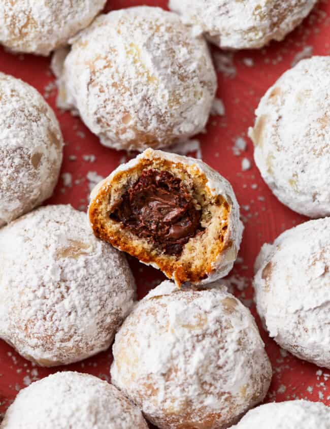 A plate of powdered sugar snowball cookies. one had a bite taken out of it to reveal a Nutella filling.