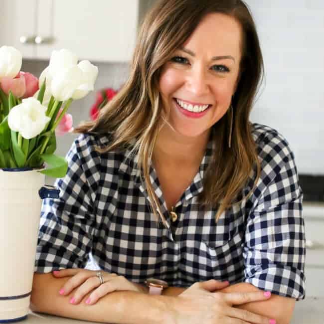 A food blogger in a plaid shirt is smiling in front of a vase of flowers.