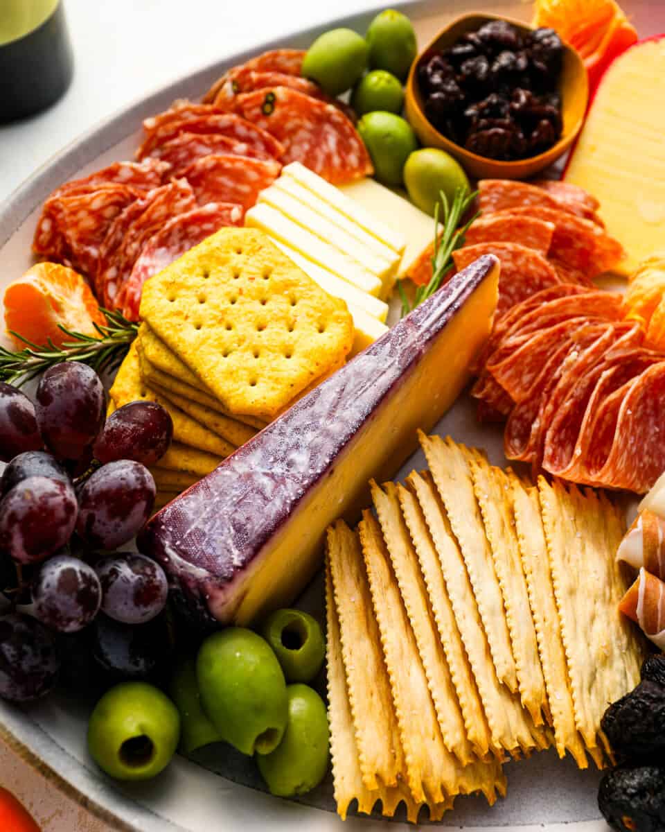 A platter of cheese, crackers, olives and grapes.