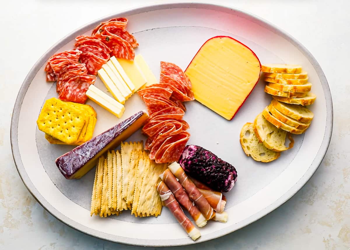A platter filled with a variety of meats, cheese, and crackers.