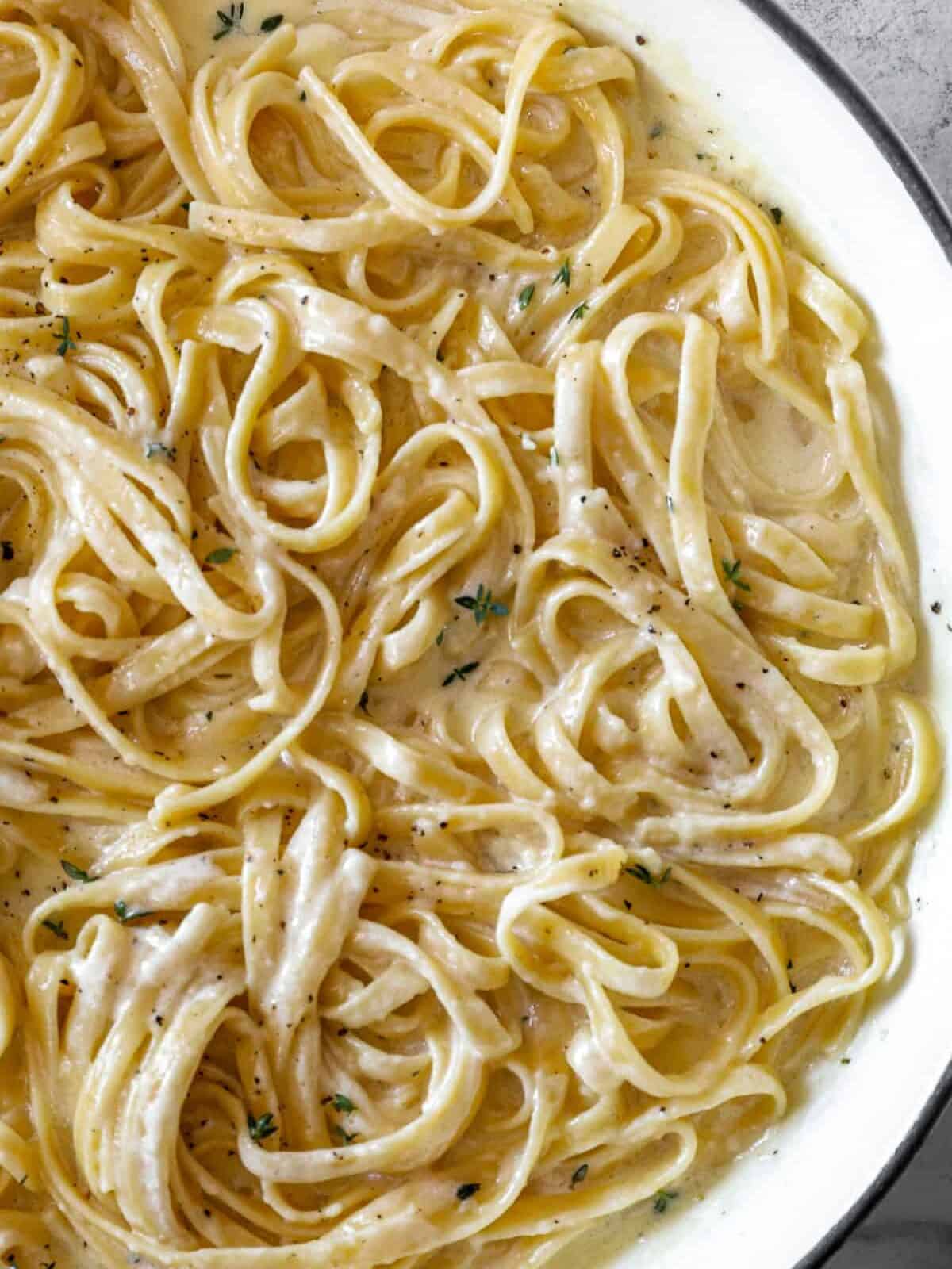 partial overhead view of fettuccini alfredo in a white dutch oven.