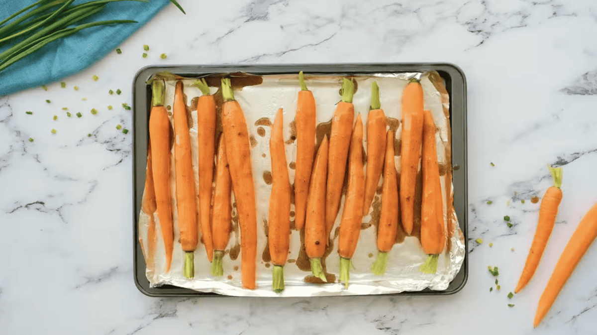carrots drizzled with spiced butter on a foil-lined baking sheet.