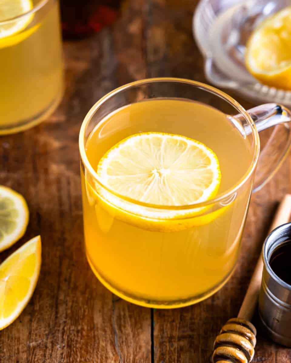 A cup of tea with lemon slices and honey on a wooden table.