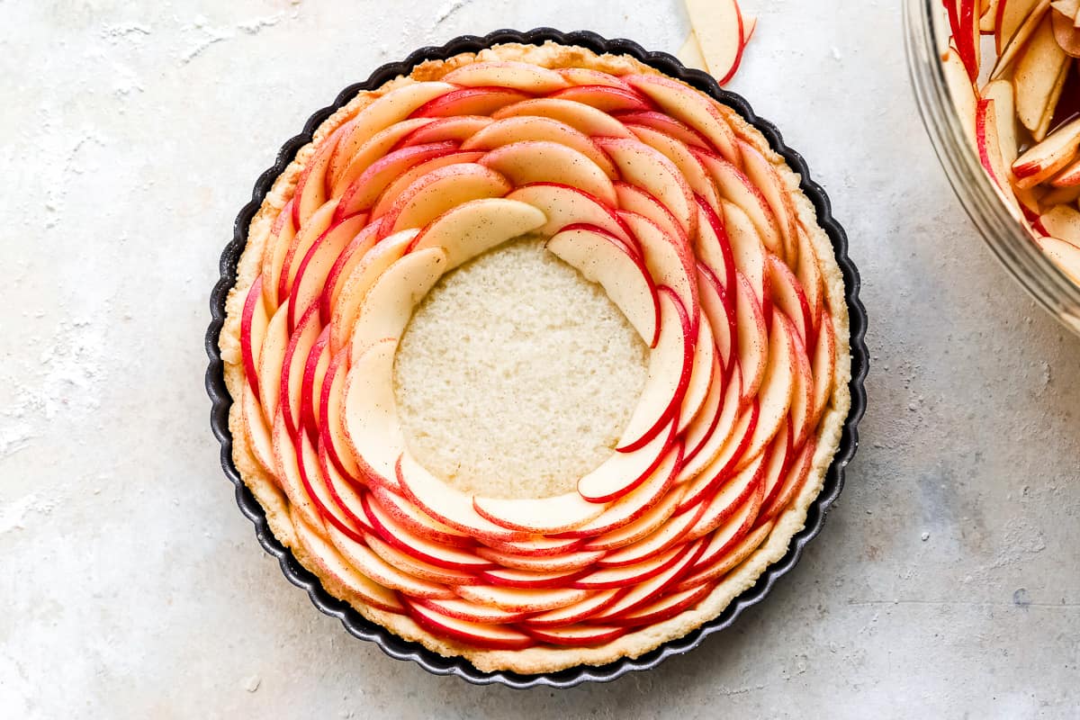 A rose apple tart in a pan with a slice of apple on top.