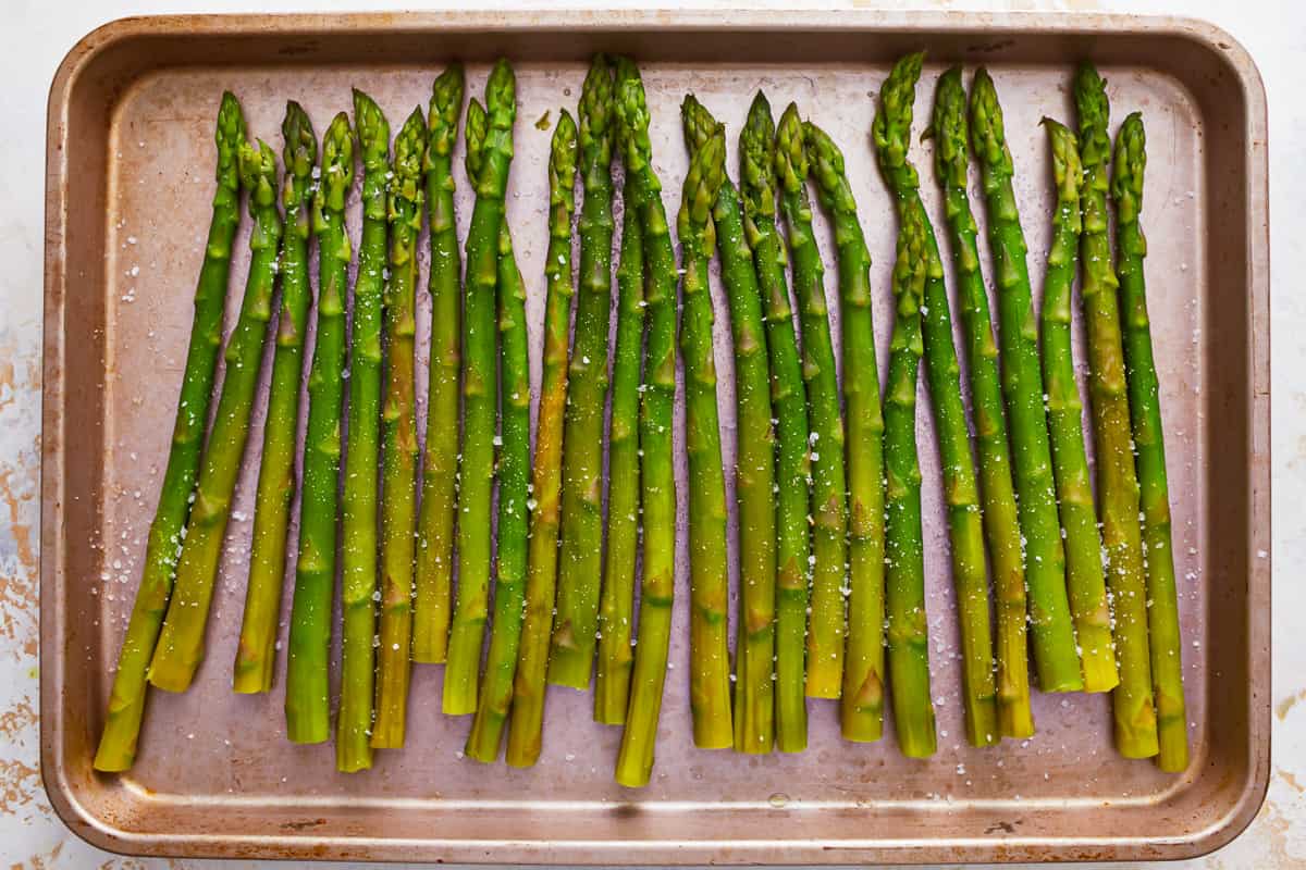Cooked asparagus spears laid out on a baking tray.