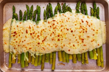 Cheesy asparagus spears on a baking sheet.