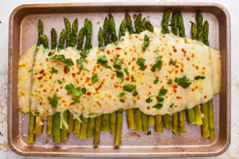 Asparagus with cheesy sauce on a baking sheet.