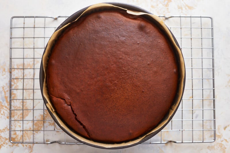 A chocolate cheesecake in a pan on a cooling rack.