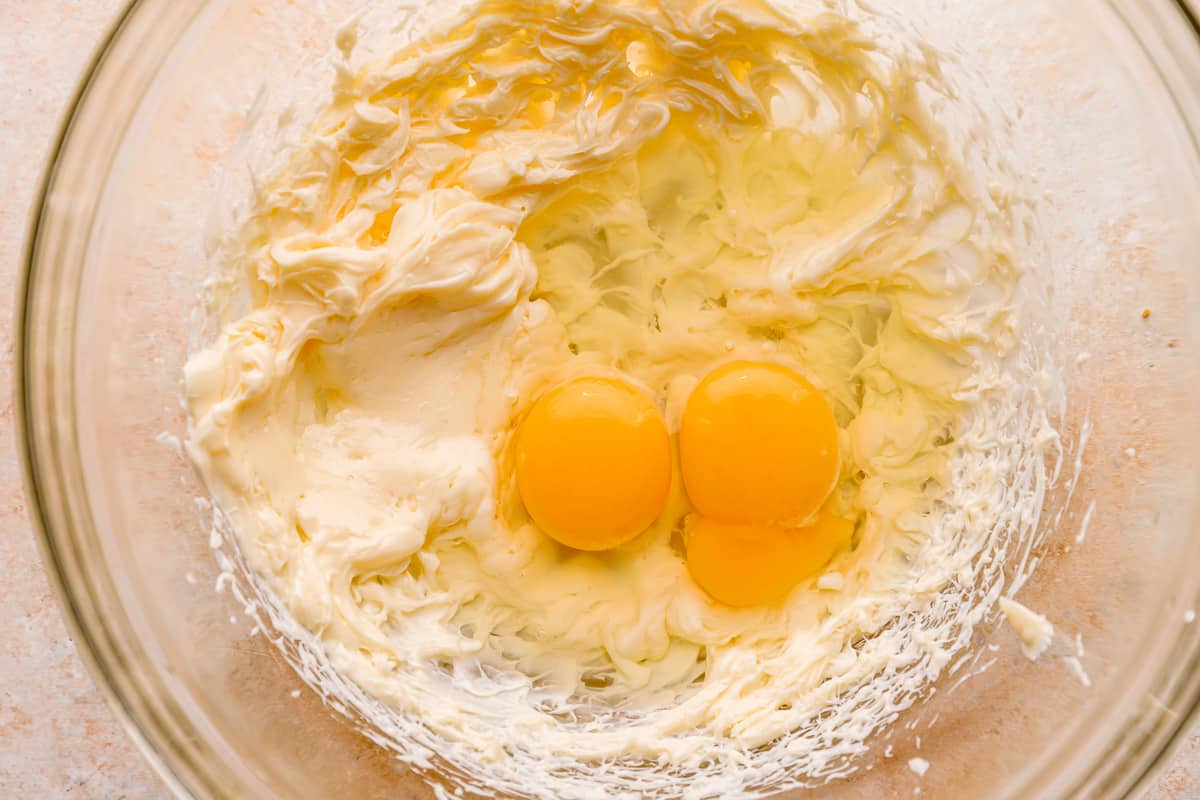 Two eggs and creamed butter in a glass mixing bowl.