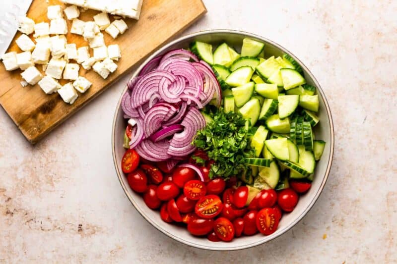sliced up cucumbers, tomatoes, and red onions in a large bowl