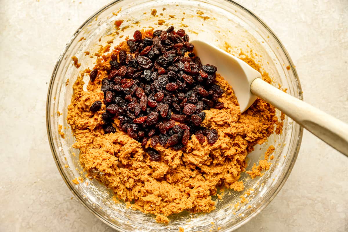 Rubber spatula mixing raisins into dough.