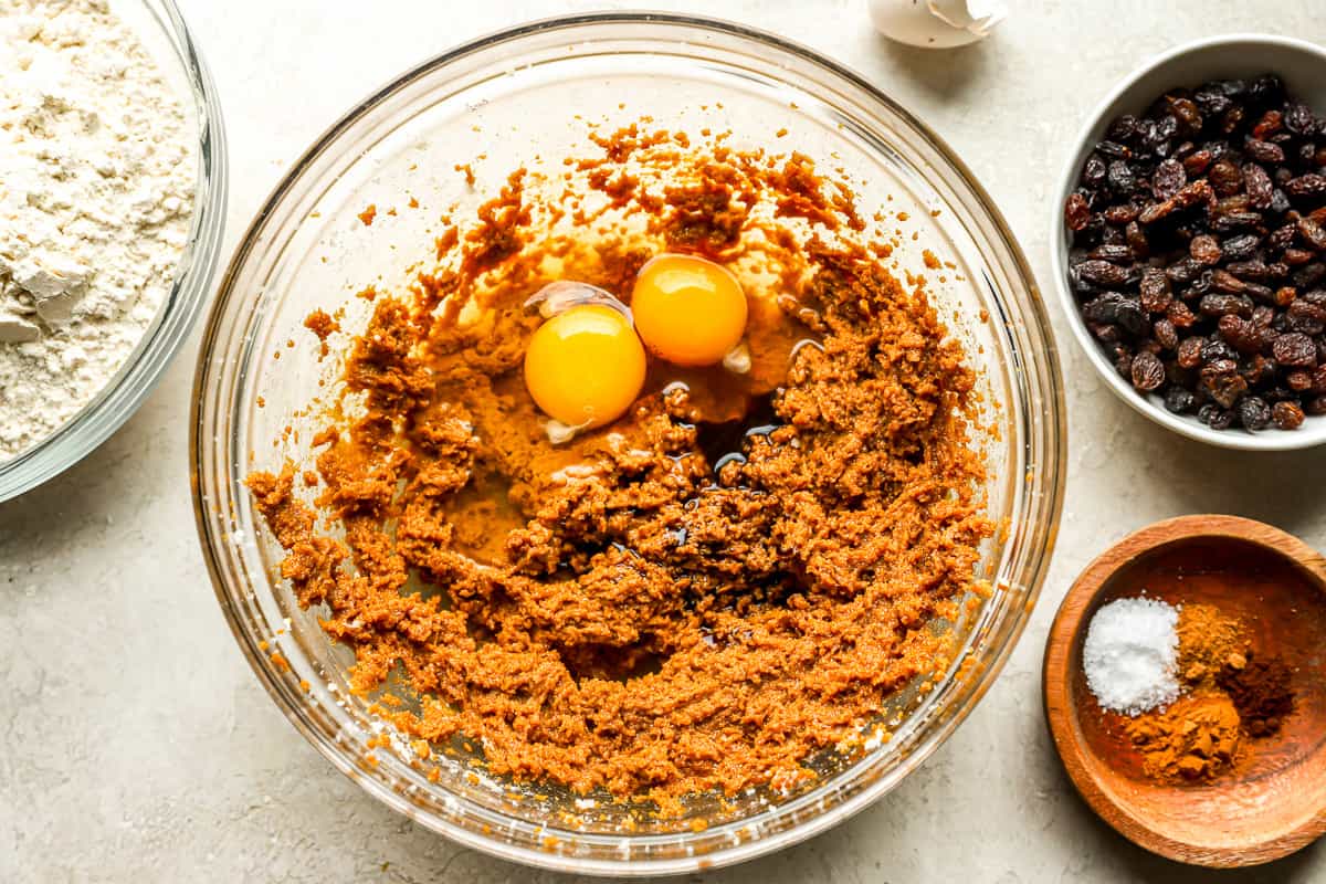 Dough ingredients in a mixing bowl with two eggs, surrounded by bowls of ingredients.