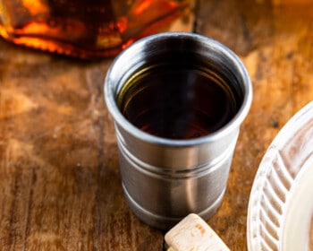 A bottle of bourbon sits on a table next to a cup of coffee.