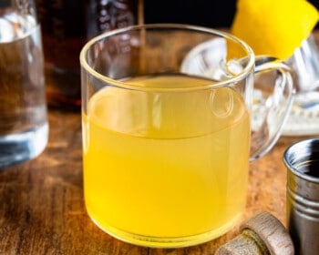 A mug of lemonade with a slice of lemon next to it.
