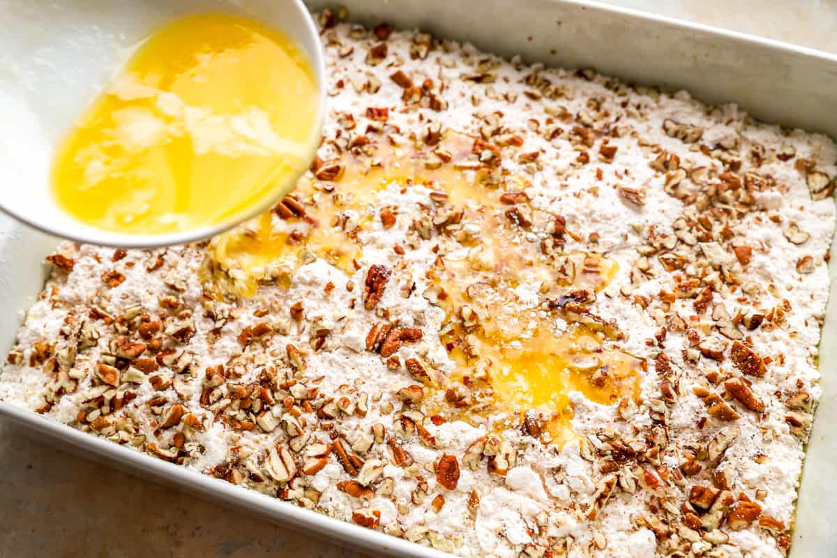 Melted butter is being poured on top of a cake topped with pecans.