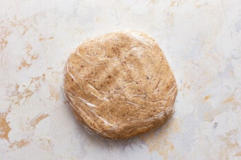 A piece of dough wrapped in plastic on a white surface.