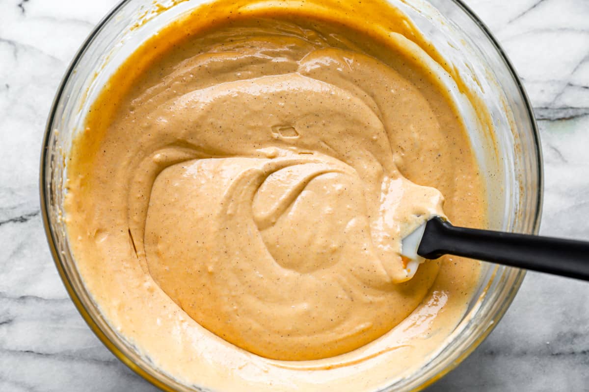 cheesecake batter in a glass bowl with a rubber spatula.