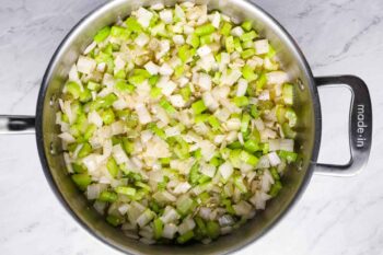 overhead view of onion, celery, and garlic cooking in a sauté pan.