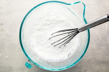 A bowl of flour with a whisk in it.