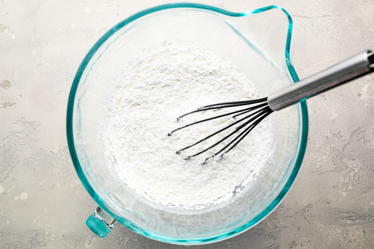 A bowl of powdered sugar with a whisk in it.