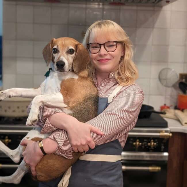 A food blogger holding a dog in a kitchen.