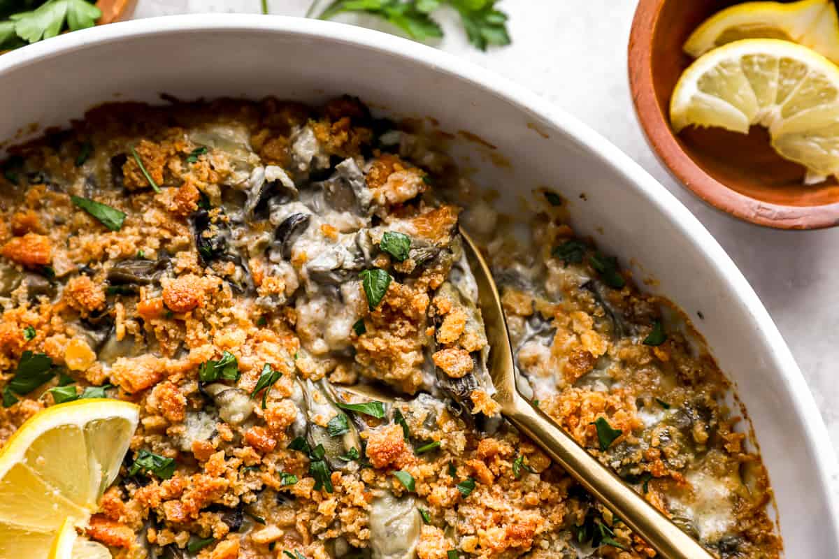 Spoon digging into a dish of oysters with a cracker topping.