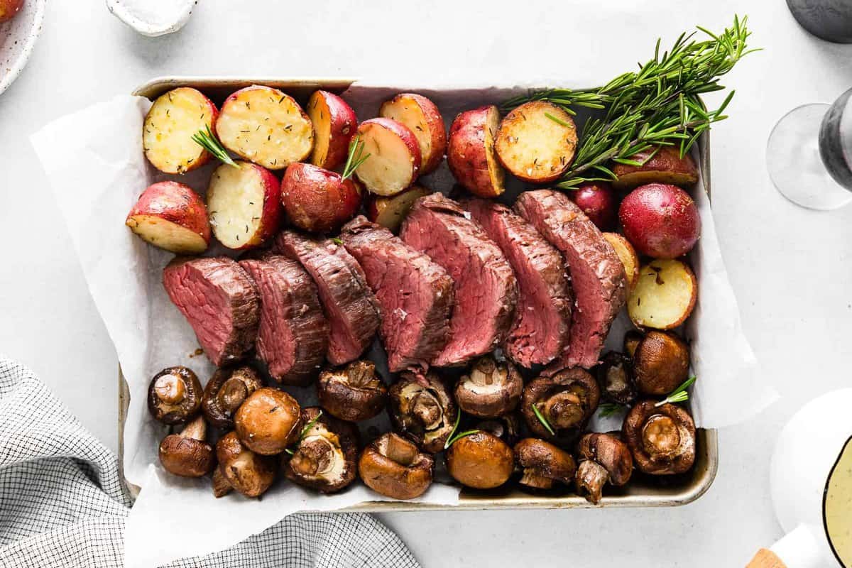 sheet pan with slices of beef tenderloin and roasted red potatoes and mushrooms