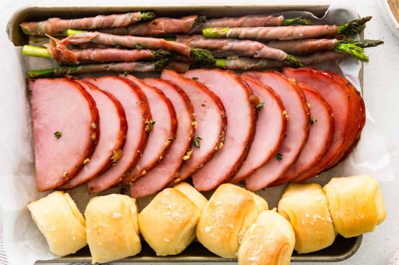 ham, prosciutto wrapped asparagus, and rolls on a sheet pan after baking