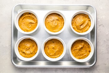 6 ramekins filled with date batter on a baking sheet.