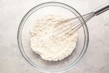 A bowl of flour with a whisk in it.