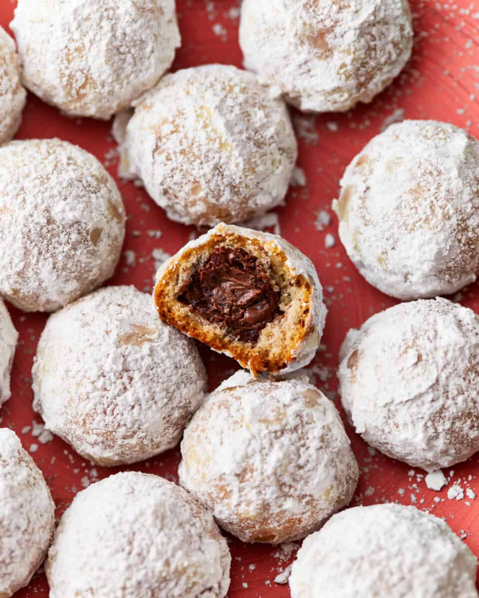 A plate of snowball cookies; one has a bite taken out to reveal the nutella stuffed inside.