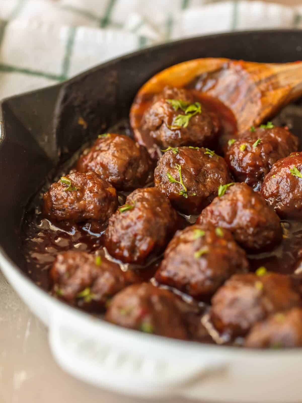 close up of cocktail meatballs in a skillet with a wooden spoon.