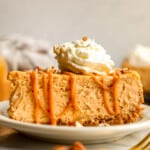 A slice of pumpkin cheesecake on a plate with whipped cream and pecans.
