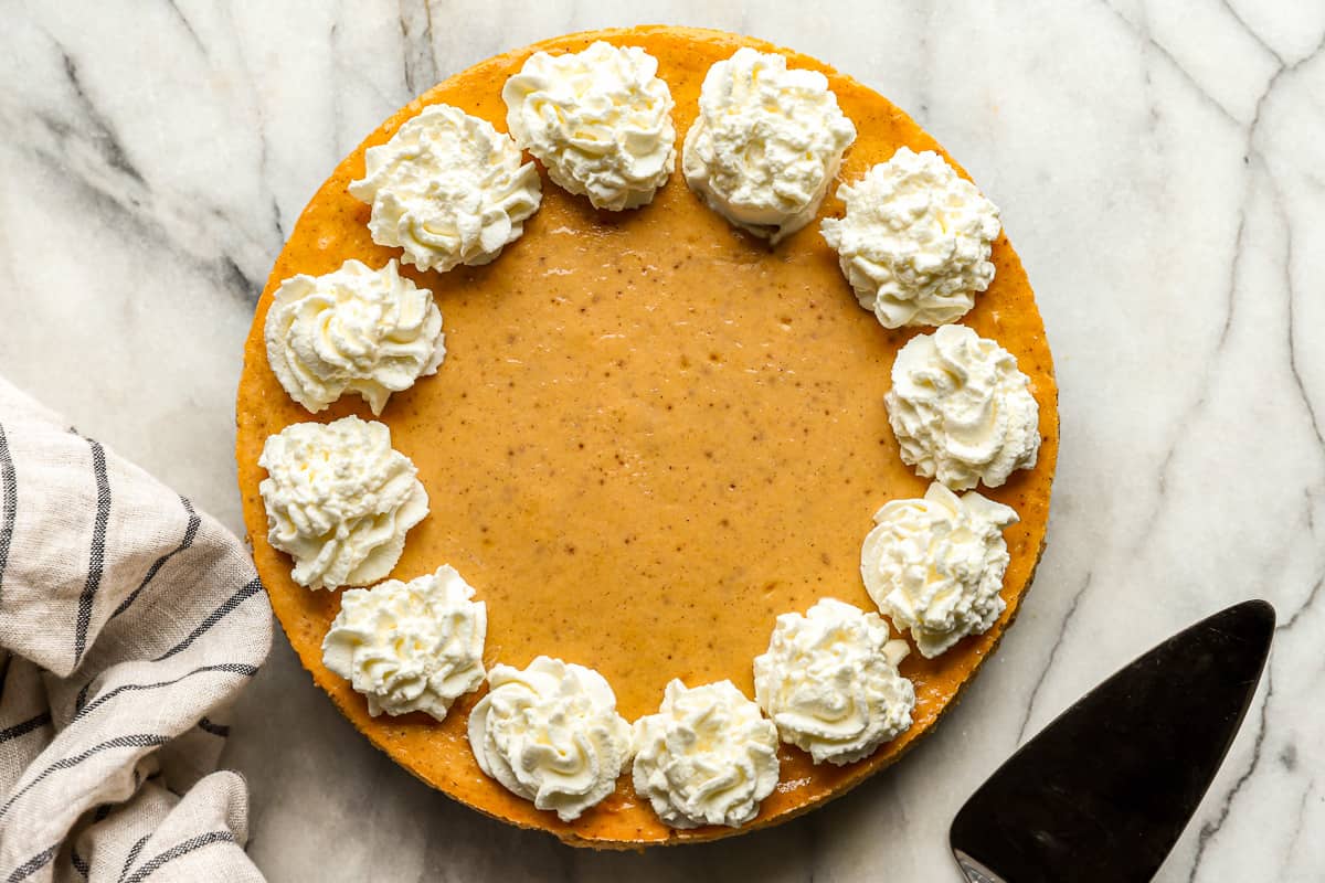 A sweet potato cheesecake topped with whipped cream and a knife.