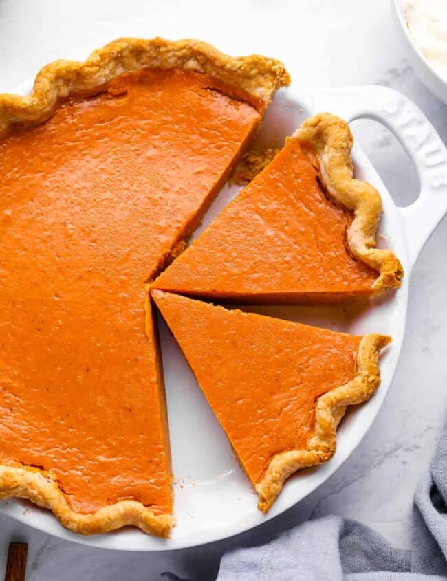 overhead view of a partially sliced sweet potato pie in a white pie pan with handles.