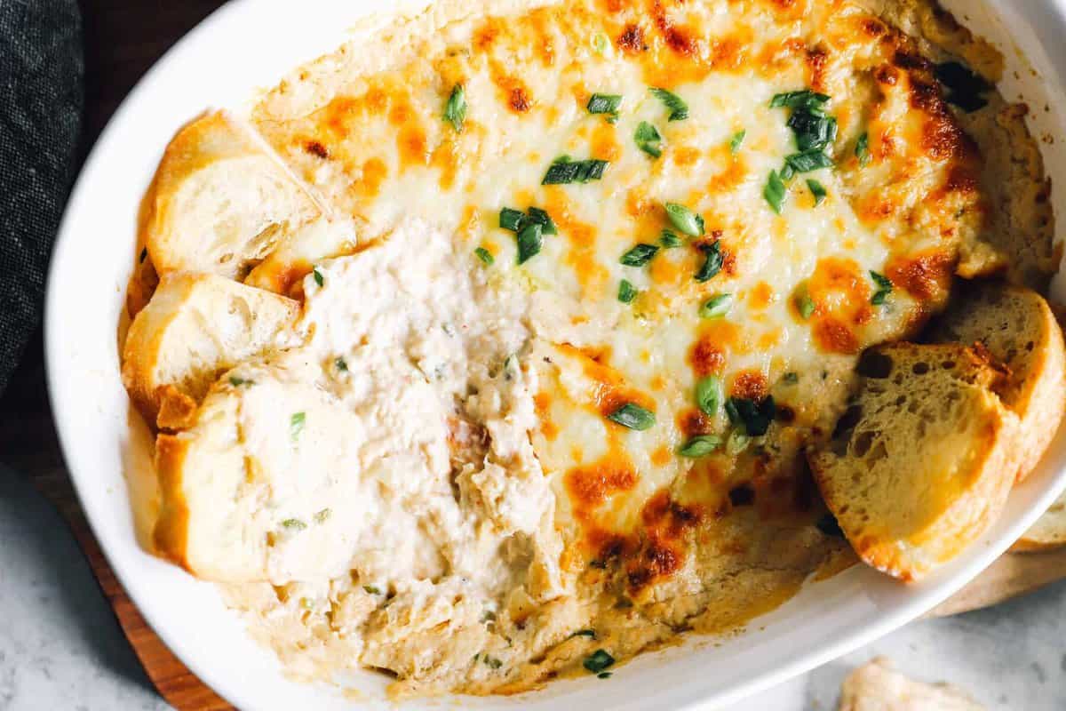 Baked hot crab dip in a baking dish with pieces of bread dipped in.