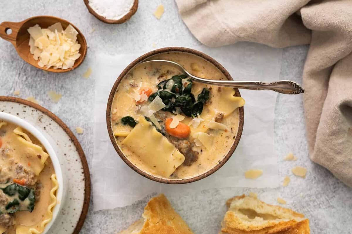 overhead view of creamy white lasagna soup in a white and brown bowl with a spoon.