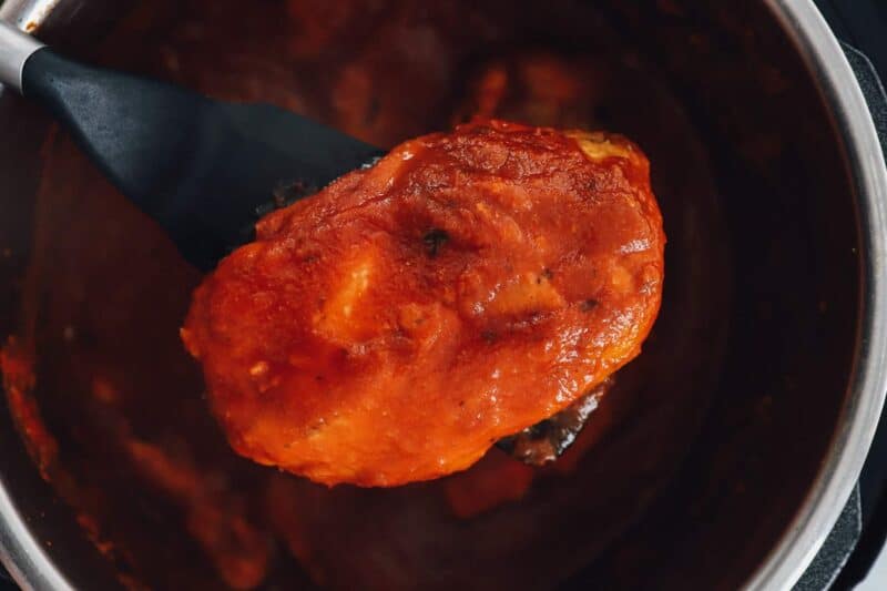 a saucy chicken breast lifted out of an instant pot.