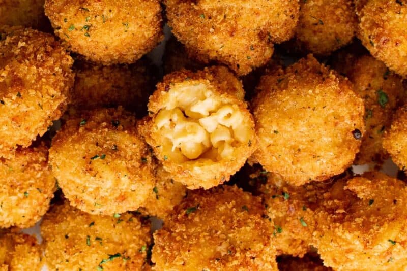 close up on fried Mac and cheese balls, the one at the center has a bite taken out to reveal the Mac and cheese