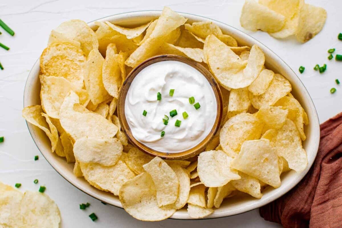 sour cream and onion dip in a small bowl on a platter of potato chips.