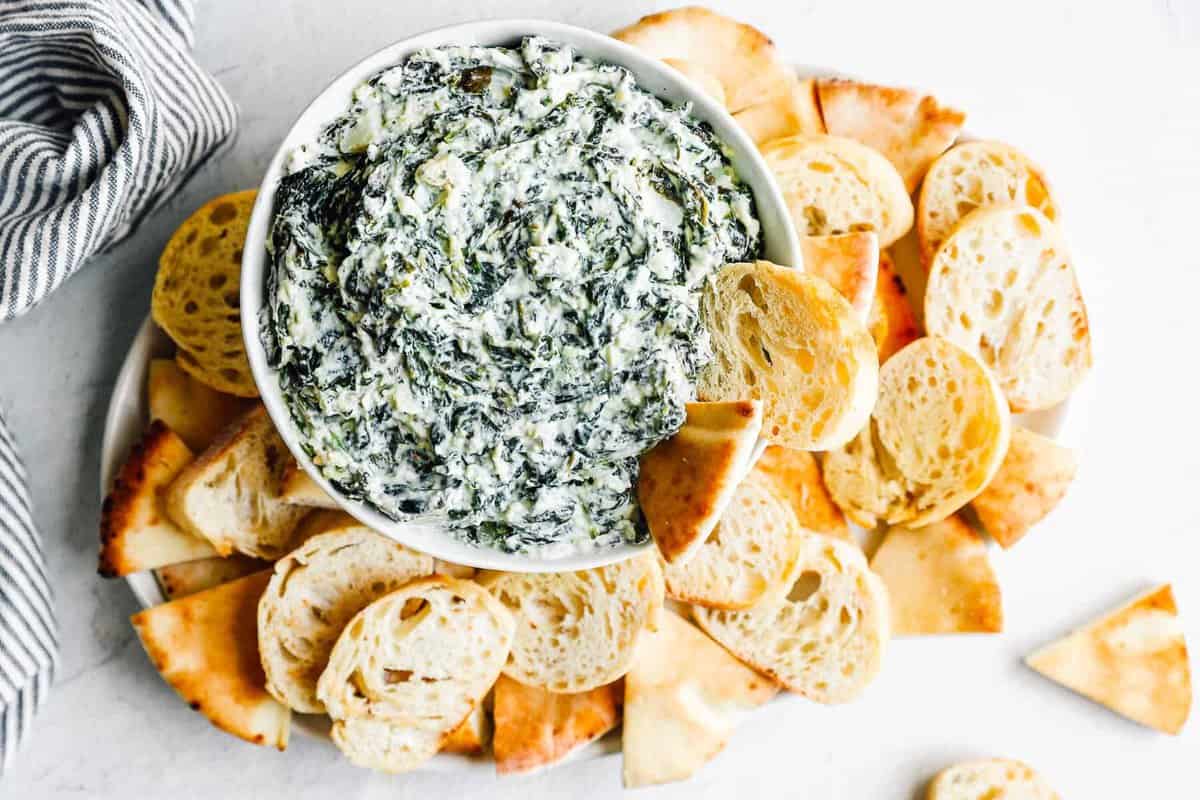 crockpot spinach dip in a white bowl with dippers