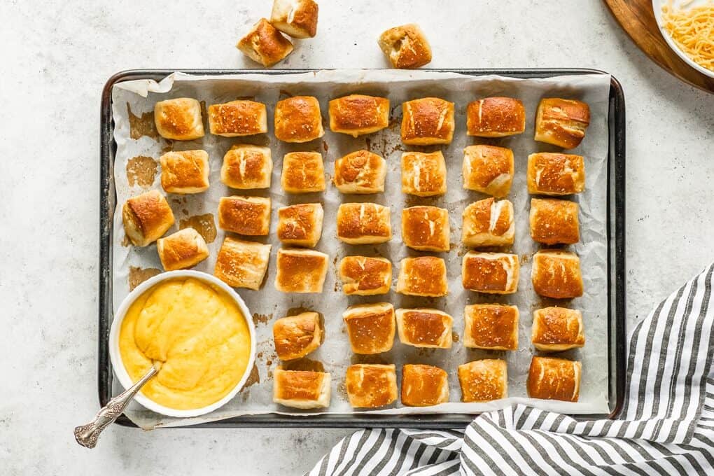 pretzel bites lined up on cookie sheet with cheese dip in bowl