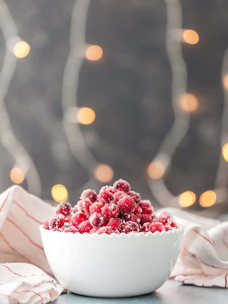 white bowl of easy sugared cranberries with white lights in background